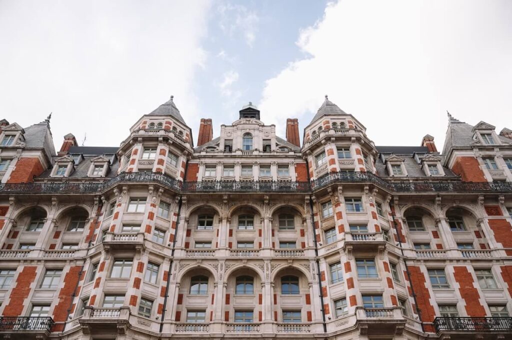 Ornate historic building with red brick and white stone details, featuring arched windows, balconies, and multiple turrets under a partly cloudy sky, viewed from a low angle.