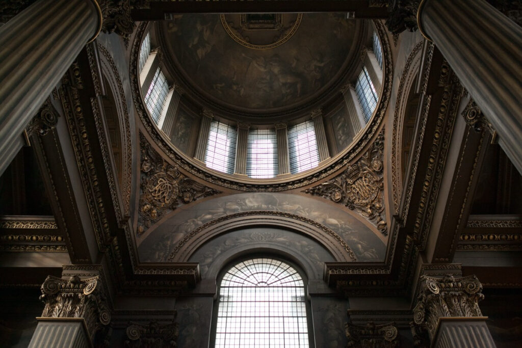 Interior view of an ornate domed ceiling with classical columns, arched windows, and detailed gold accents, showcasing intricate architectural and artistic design elements in a grand historical building.